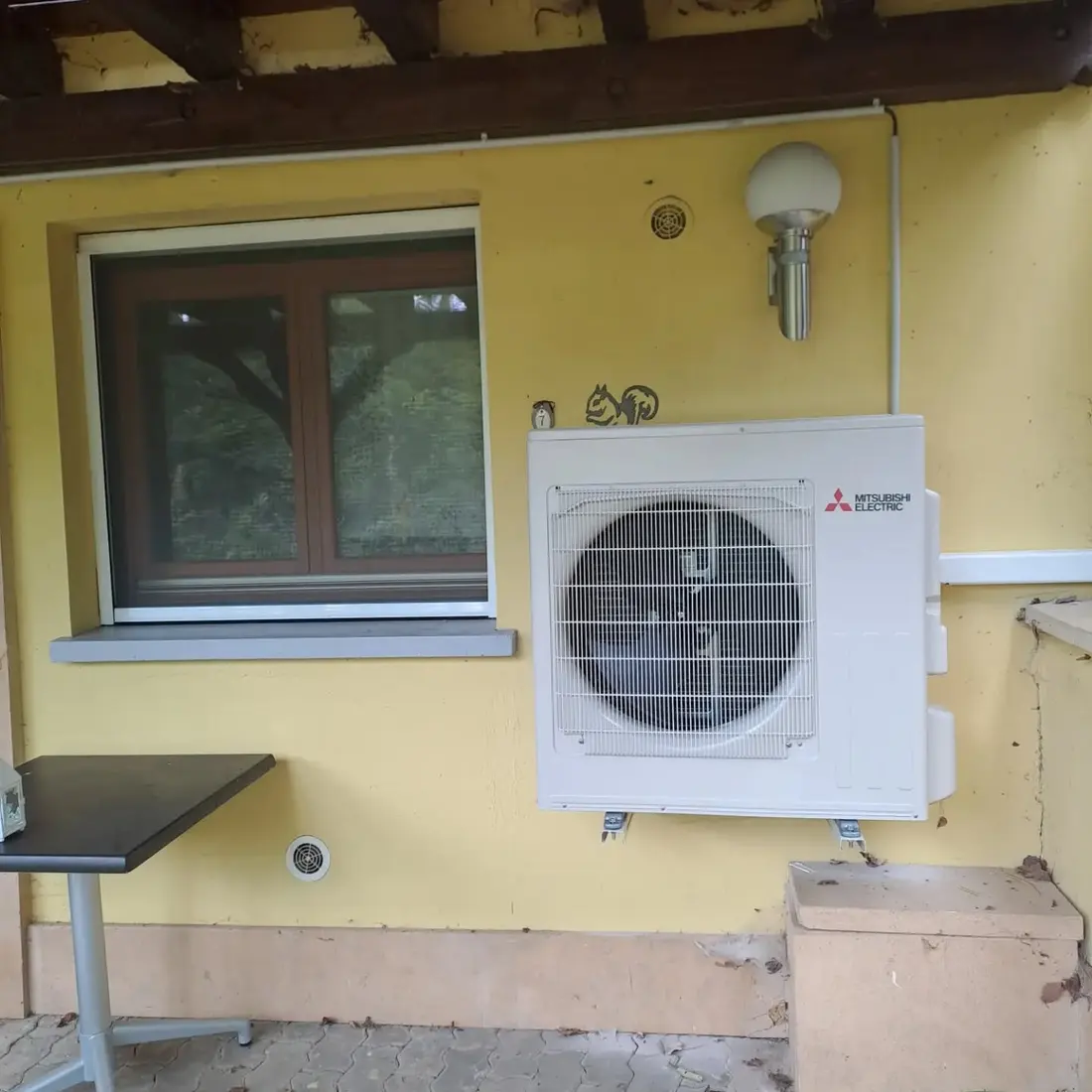 Groupe extérieur Mitsubishi Electric fixé sur consoles murales, sous un auvent en façade