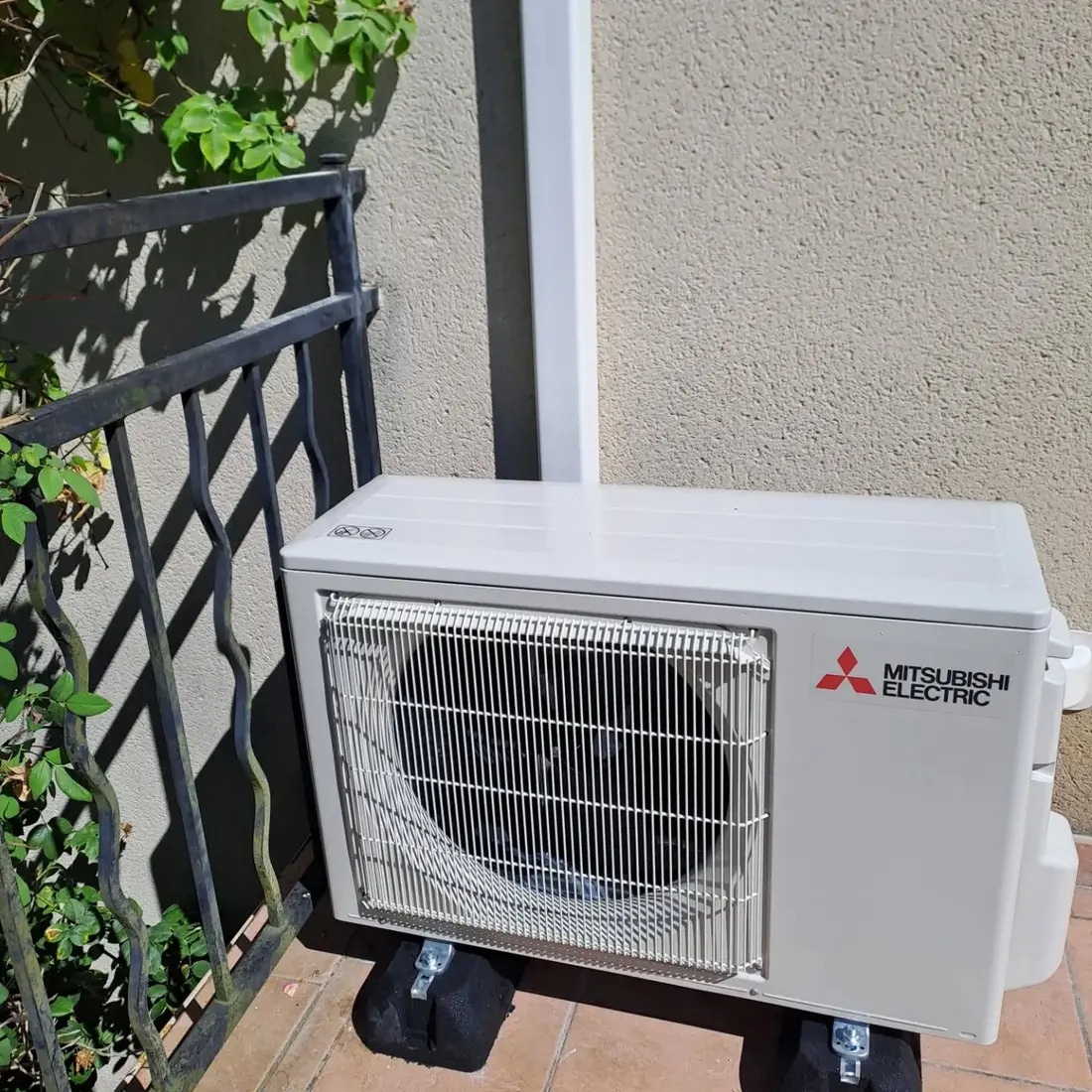 Groupe extérieur Mitsubishi Electric posé sur plots antivibratiles en terrasse, goulotte verticale blanche le long de la façade